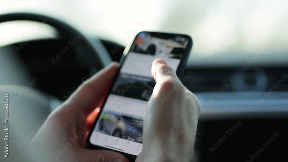 Shopping for a new luxury car online looking at different models on smartphone mobile phone. Driver looks at the new cars store, sitting in the car. Smart phone online shopping. Watch ads from car