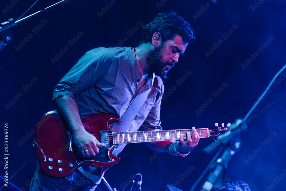 Obraz premium Musician playing electric guitar during rock band live concert. Black hair male guitar player performing on stage. Music lights show