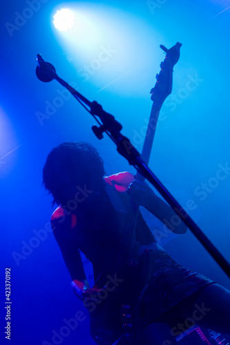 Unrecognizable female short hair guitarrist. Music lights show silhouette during rock band live concert. Foggy light