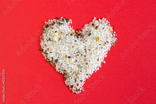 Spices, white, black and red peppers, sea salt sprinkled on bright red background, close-up heart shape