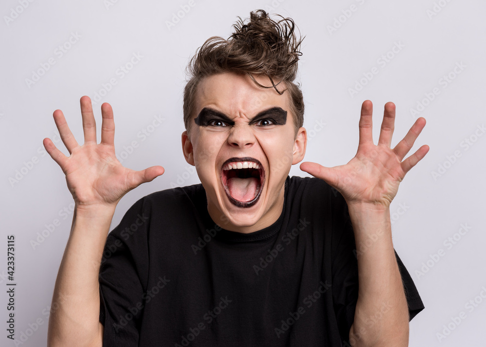 Crazy teen boy with spooking make-up making horns with fingers, isolated on white background. Teenager in style of punk goth dressed in black screaming and shouting. Problems of transitional age Crazy teen boy with spooking make-up making horns with fingers, isolated on white background. Teenager in style of punk goth dressed in black screaming and shouting. Problems of transitional age