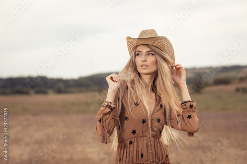 Girl in a bohemian style in the steppe. Blonde girl with a hat on the prairie.