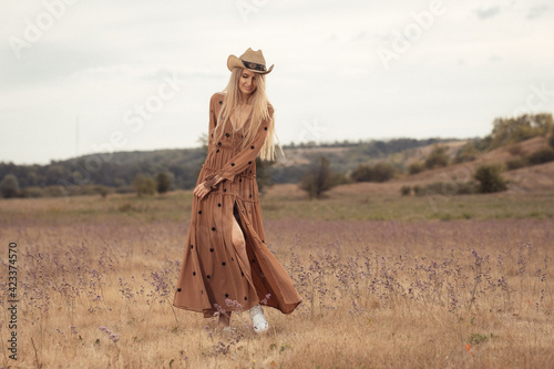 Girl in a bohemian style in the steppe. Blonde girl with a hat on the prairie.