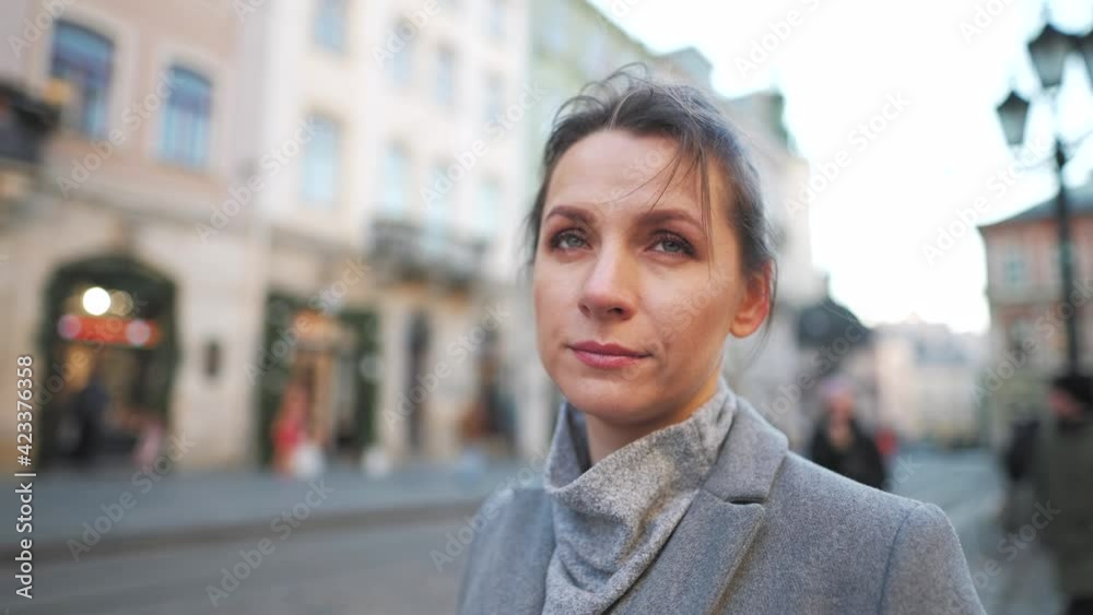 Portrait of a Caucasian woman in a coat in the middle of the old city square. She looking seriously at the camera. Slow motion Portrait of a Caucasian woman in a coat in the middle of the old city square. She looking seriously at the camera. Slow motion