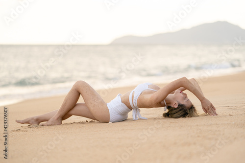 Woman in bikini lying down on sand beach relaxing sunbathing.