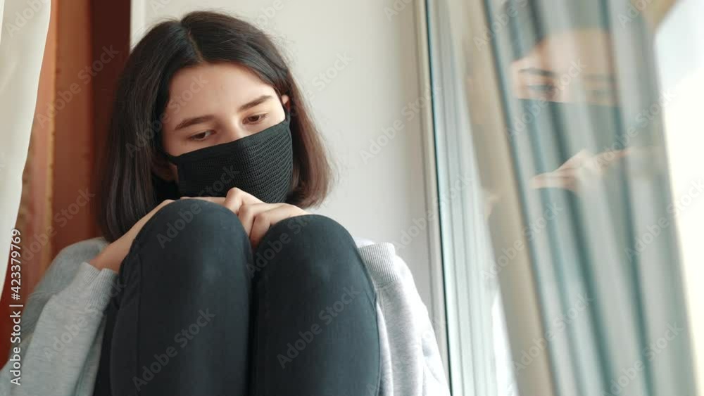 coronavirus. girl kid looks out window sad in a medical mask. stay at home. covid pandemic self-isolation coronavirus infection stay home concept. kid mask touches window wants to go outdoor coronavirus. girl kid looks out window sad in a medical mask. stay at home. covid pandemic self-isolation coronavirus infection stay home concept. kid mask touches window wants to go outdoor