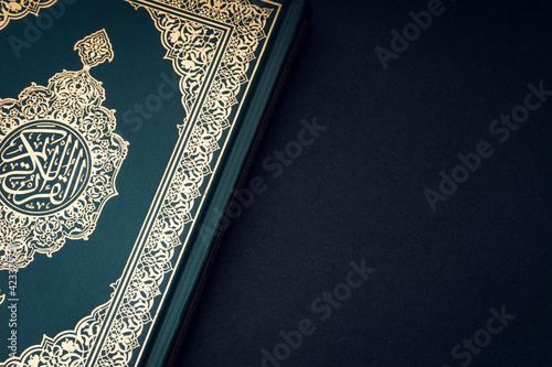 Holy Al Quran with written arabic calligraphy meaning of Al Quran on black background. Copy space and crop fragment