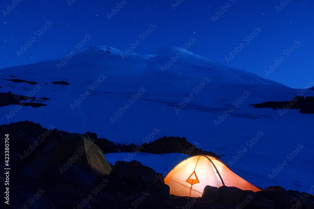 Glowing tent in front of night Elbrus at starry night. Prielbrusye National Park, Kabardino-Balkaria, Caucasus, Russia.