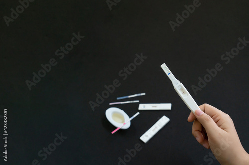 Urine Pregnancy test as midstream style HCG test holding by woman hand with copy space on black background. New life and new family concept.