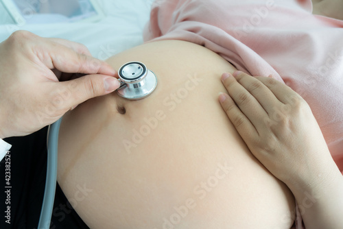Pregnant woman visiting baby doctor for examine. Doctor hand using stethoscope for examine belly of pragnant woman in a hospital or clinic.