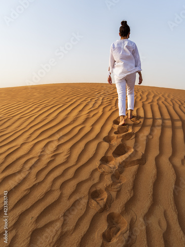Woman walking uphill in a sand dune in the Dubai desert leaving footprints
