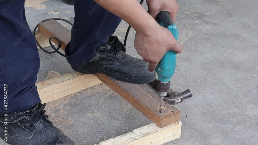 Man used electric drill is drilling wooden bar for making wooden pallet in work area closeup. Man used electric drill is drilling wooden bar for making wooden pallet in work area closeup.