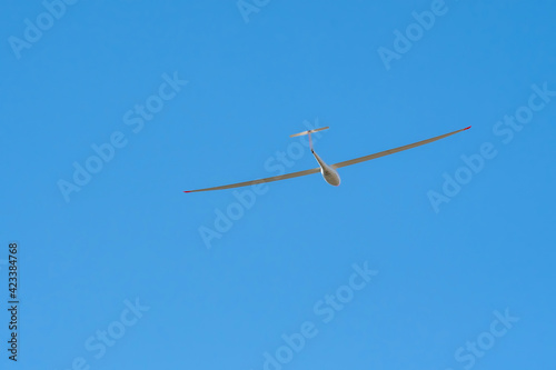 A Glider (sailplane) soaring on the background of blue sky on sunny day.