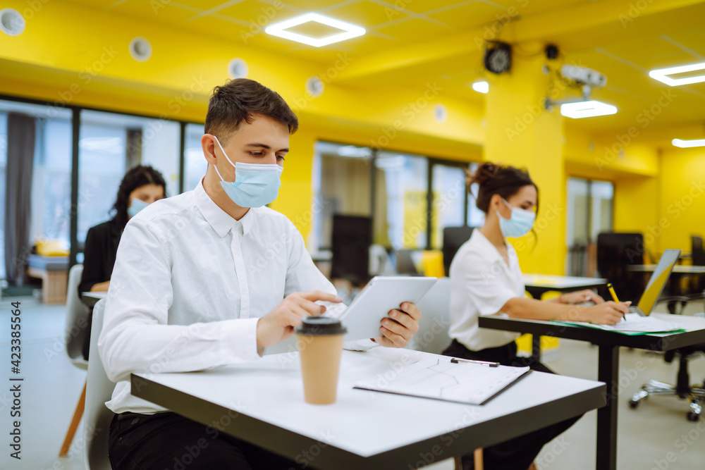 Office worker wearing medical face mask for social distancing for virus prevention while using laptop back at work in office. Teamwork Process during pandemic in quarantine. Covid-19. Office worker wearing medical face mask for social distancing for virus prevention while using laptop back at work in office. Teamwork Process during pandemic in quarantine. Covid-19.