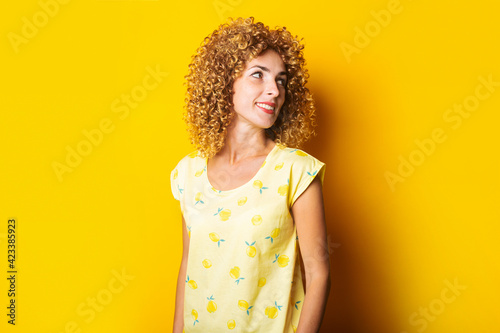 cute curly girl smiling looks to the side on a yellow background.