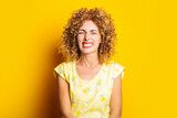 curly young woman with closed eyes grimaced against yellow background