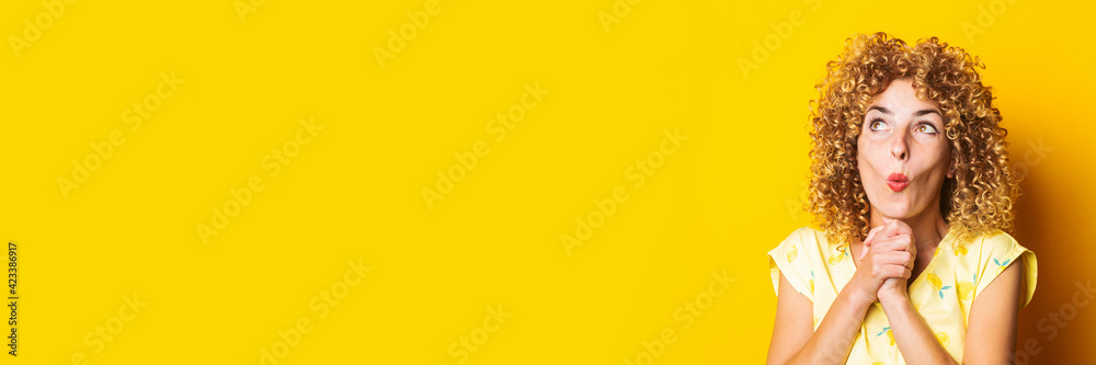 surprised shocked curly young woman with clasped hands under the chin on a yellow background. Banner surprised shocked curly young woman with clasped hands under the chin on a yellow background. Banner