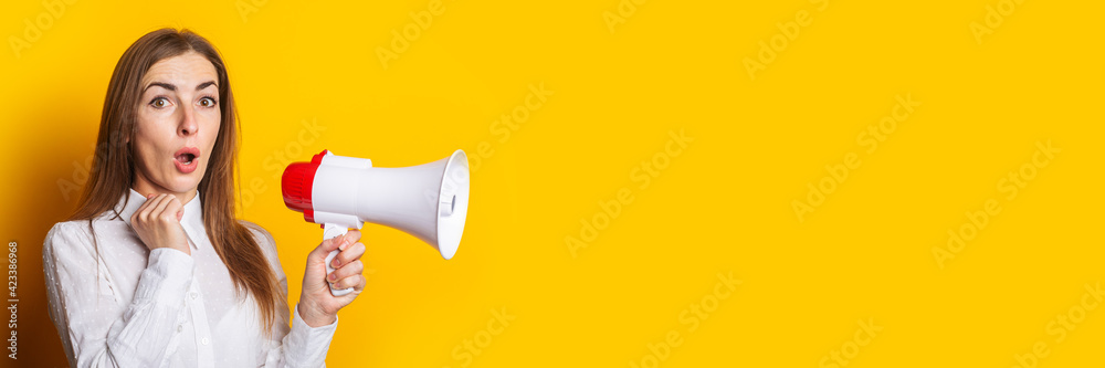 Surprised young woman in a white shirt holds a megaphone on a yellow background. Hiring concept, ad Surprised young woman in a white shirt holds a megaphone on a yellow background. Hiring concept, ad