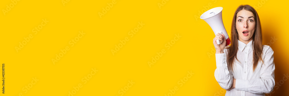 Surprised woman holding a megaphone in her hands on a yellow background. Hiring concept, help wanted. Banner Surprised woman holding a megaphone in her hands on a yellow background. Hiring concept, help wanted. Banner