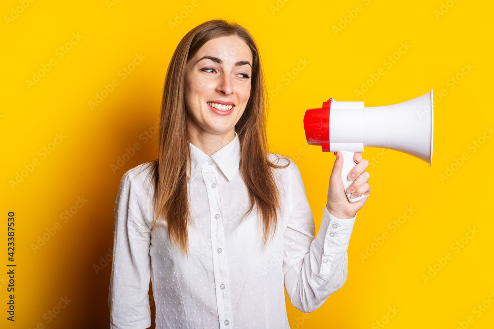 Friendly young woman holds a megaphone in her hands on a yellow background. Hiring concept, help wanted. Banner Friendly young woman holds a megaphone in her hands on a yellow background. Hiring concept, help wanted. Banner