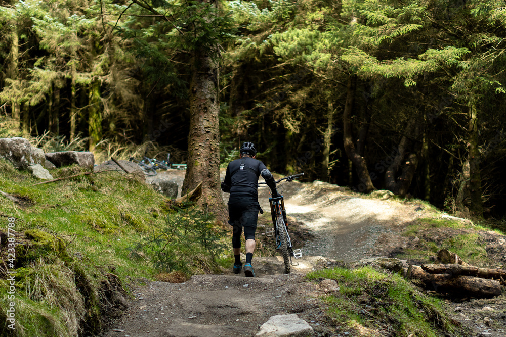 Mountain bike cyclist from back walking through forest