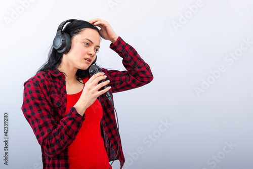 cheerful young woman in casual clothes with headphones sing song in microphone, mock up, copy space