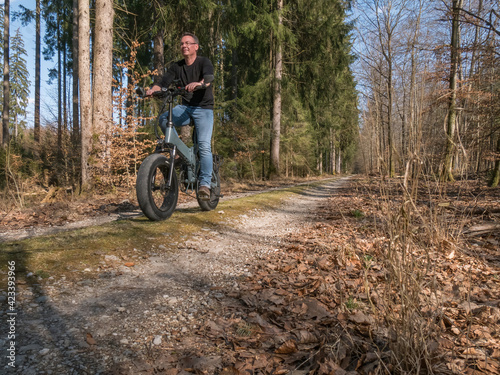 Young man riding on modern big E-bike through the forest