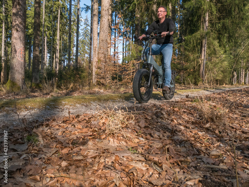 Young man riding modern E-bike on path through the forest 