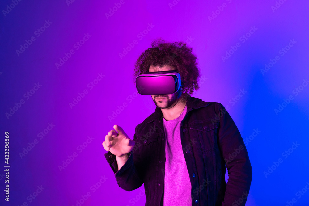 Hipster young man using virtual reality headset over blue purple background. Concept of hi tech and modern technology. Hipster young man using virtual reality headset over blue purple background. Concept of hi tech and modern technology.