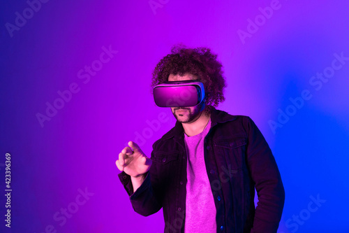Hipster young man using virtual reality headset over blue purple background. Concept of hi tech and modern technology.