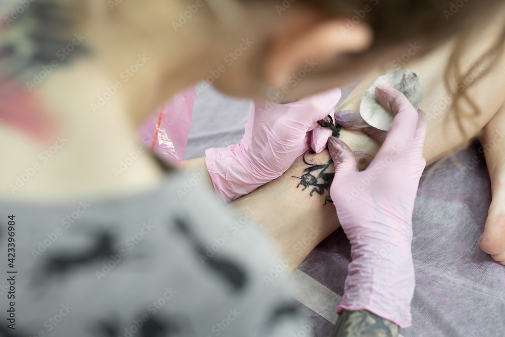 Obraz premium Close-up of a tattoo artist doing a tattoo on the leg of a young girl in the salon. Professional tattooist doing tattooing in studio
