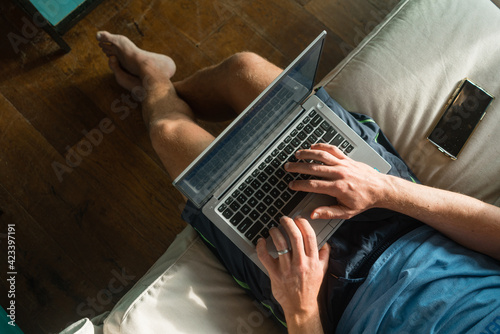Overhead view of man working from home on a laptop computer while sitting on a sofa