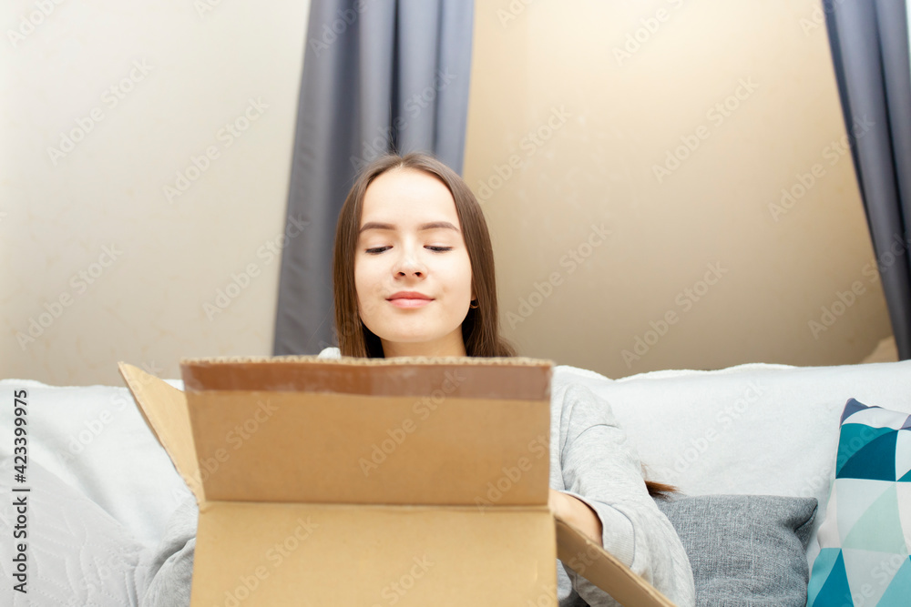 A young woman opens a box with an order. The concept of online shopping and delivery of goods A young woman opens a box with an order. The concept of online shopping and delivery of goods