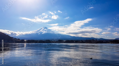 An idyllic view on Mt Fuji from the side of Kawaguchiko Lake, Japan. The magnificent mountain is surrounded by clouds. Soft reflections in the calm surface of the lake. Serenity and calmness