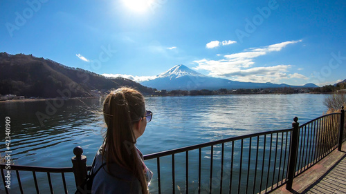 Woman walking across the bridge next to Kawaguchiko Lake, Japan with the view on Mt Fuji. The mountain is surrounded by clouds. Girl is enjoying the walk and good weather. Serenity and calmness