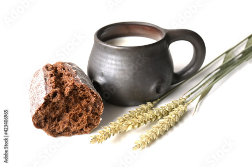 Fresh cow's milk in a ceramic mug,  grain bread and three bread spikelets on a white background. Morning breakfast. Healthy and ecological food.