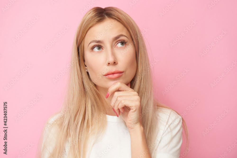 Pensive young woman holding chin in doubt portrait. thinking creative person in white shirt, dreamy girl thought and looking up isolated on pink studio background Pensive young woman holding chin in doubt portrait. thinking creative person in white shirt, dreamy girl thought and looking up isolated on pink studio background