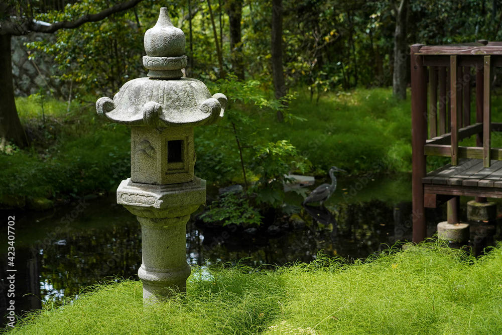 Japanese traditional lantern near small river or canal in Japanese garden,egret bird on background with old terrace nearby in Japan.