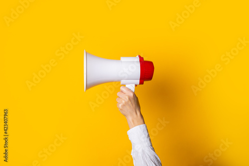 female hand holds a white with a red megaphone on a yellow background.