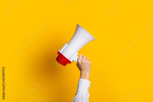 Female hand holds a white with a red megaphone on a yellow background.