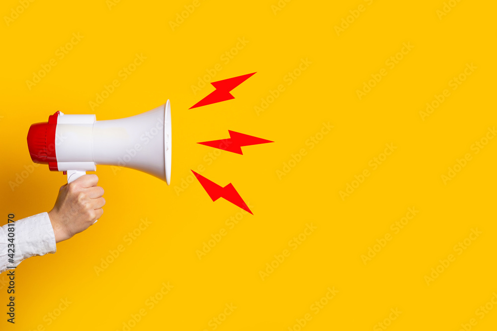 female hand holds a megaphone on a yellow background, added picture sound - obrazy, fototapety, plakaty 