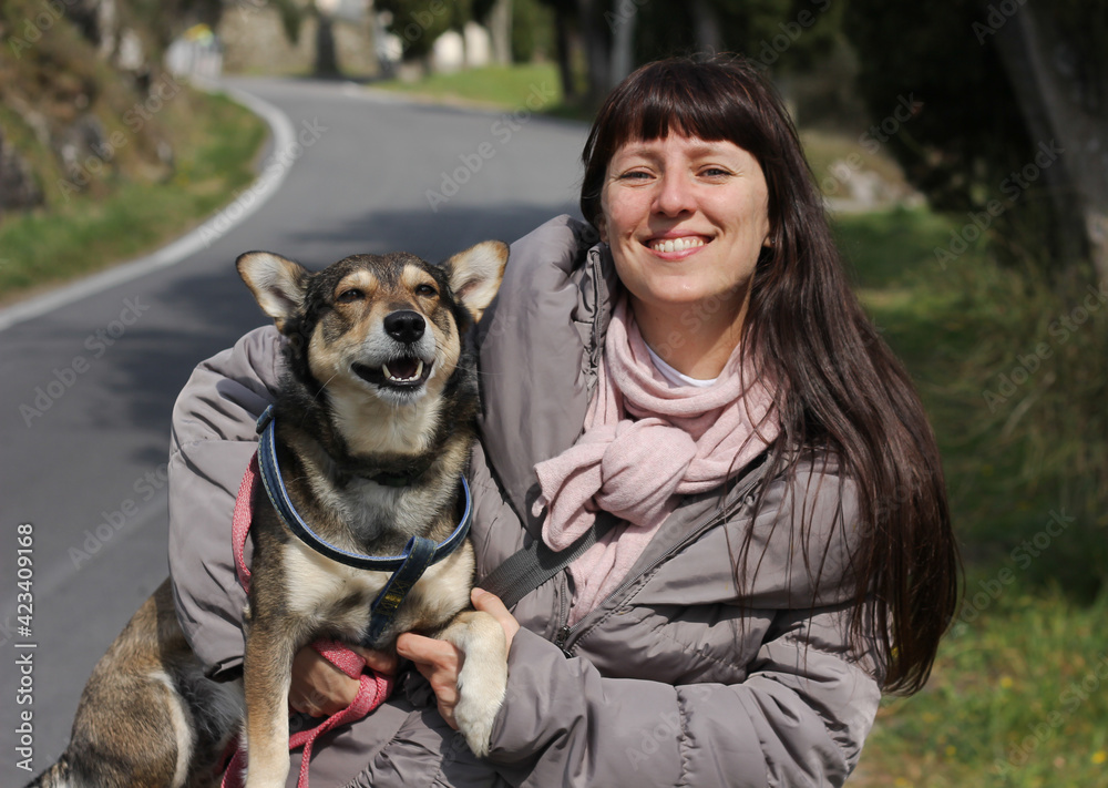 Smiling girl with a happy dog in her arms. The dog was taken from the animal shelter. On a blurred background of the road and nature. Smiling girl with a happy dog in her arms. The dog was taken from the animal shelter. On a blurred background of the road and nature.