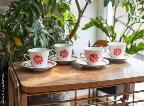 Mid-century modern porcelain cups with red pattern, on a wooden table with plants in the background
