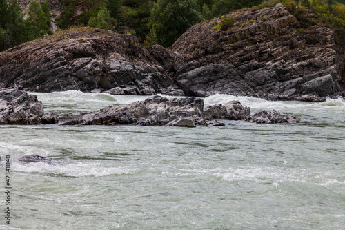 A close-up of a fast-flowing mountain river Katun with a large rock in the middle is a dangerous obstacle in the path of rafting rafters. Nature and water. © Aleksandr Kondratov