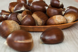 Ripe chestnuts on a plate on wooden background. Selective focus