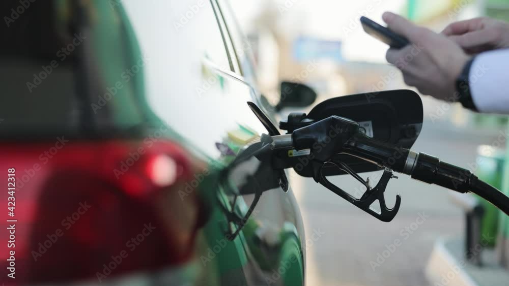 Businessman uses a mobile application in a smartphone to pay for refueling a car. Closeup of man filling benzine gasoline fuel in car at gas station. Man Refueling Car At Gas Station