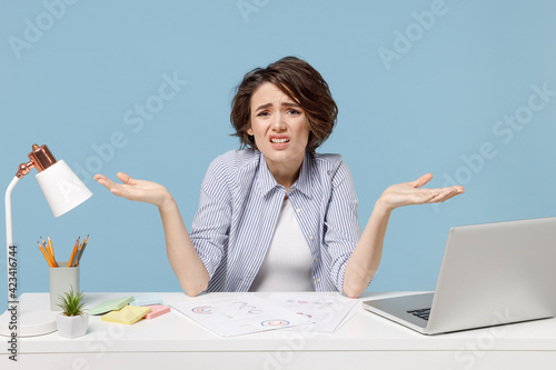 Cuadro en lienzo Young confused mistaken disappointed employee business director woman 20s wearing casual shirt sit work at white office desk with pc laptop spreading hands isolated on pastel blue background studio
