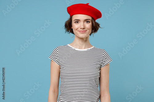 Young caucasian smiling woman 20s with short hairdo wearing french beret red hat striped t-shirt look aside isolated on pastel blue color background studio portrait. People lifestyle fashion concept. photo