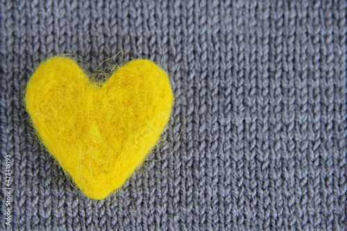 A yellow heart made of wool lies on a gray knitted background.The concept of handmade  needlework  Valentine s day.The colors of 2021 are gray and yellow. Top view.Flat styling style.Copyspace
