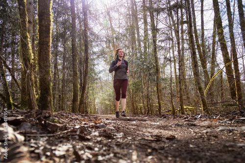 Caucasian Woman Trail Running in the Green Forest surrounded by beautiful trees. Taken in Squamish, British Columbia, Canada.